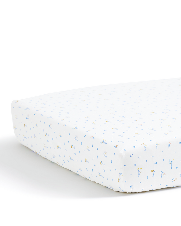 A close-up of the Luxe Premium Percale Crib Sheet in Letters and Lullabies, featuring a white background adorned with small, light blue and yellow animal prints on a crib mattress.