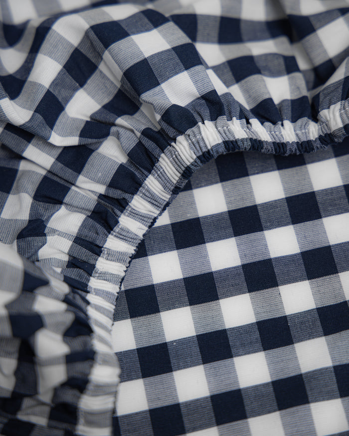 Featuring a close-up of the ultra-soft Luxe Premium Cotton Navy Gingham Crib Sheet by Petite Plume, this elastic-gathered sheet shows creases and ruffles. Its prominent texture highlights the classic navy gingham check pattern.