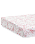 A close-up of the Luxe Premium Percale Crib Sheet in Pink Timeless Toile, featuring a red and white floral toile pattern. The fitted sheet hugs the mattress snugly, with corners neatly tucked in.
