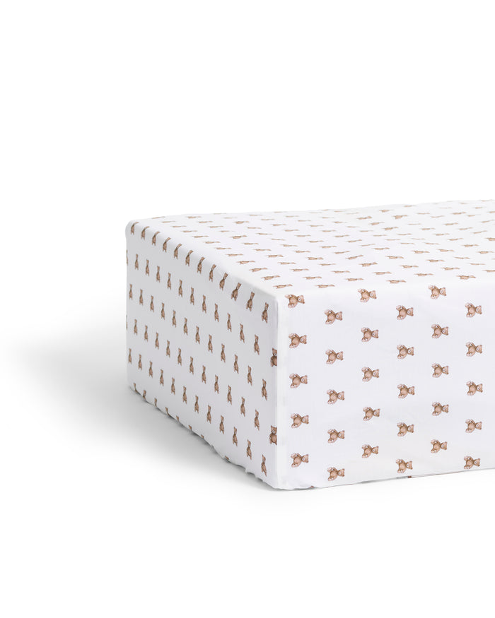 A close-up of the Luxe Premium Percale Crib Sheet in Teddy Tales, featuring a small repeating brown and orange floral pattern on white, smoothly wrapped around a mattress corner.