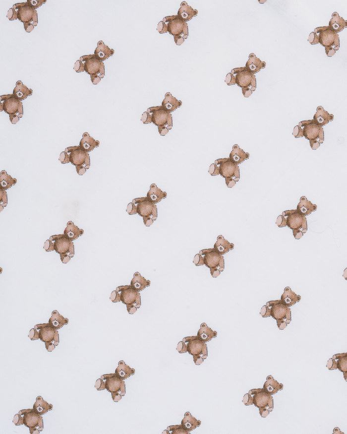 A close-up of the Luxe Premium Percale Crib Sheet in Teddy Tales, featuring a small repeating brown and orange floral pattern on white, smoothly wrapped around a mattress corner.