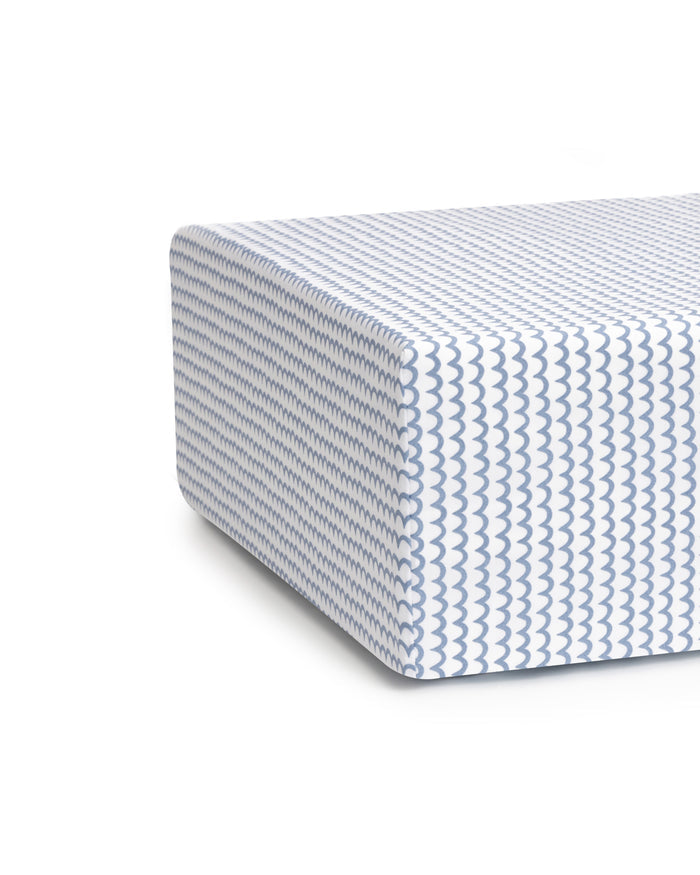 Close-up of Luxe Premium La Mer Crib Sheet by Petite Plume, showcasing an ultra-soft white fabric with a blue wave pattern. The sheet resembles a thick, modern mattress corner and sits on a breathable white backdrop.