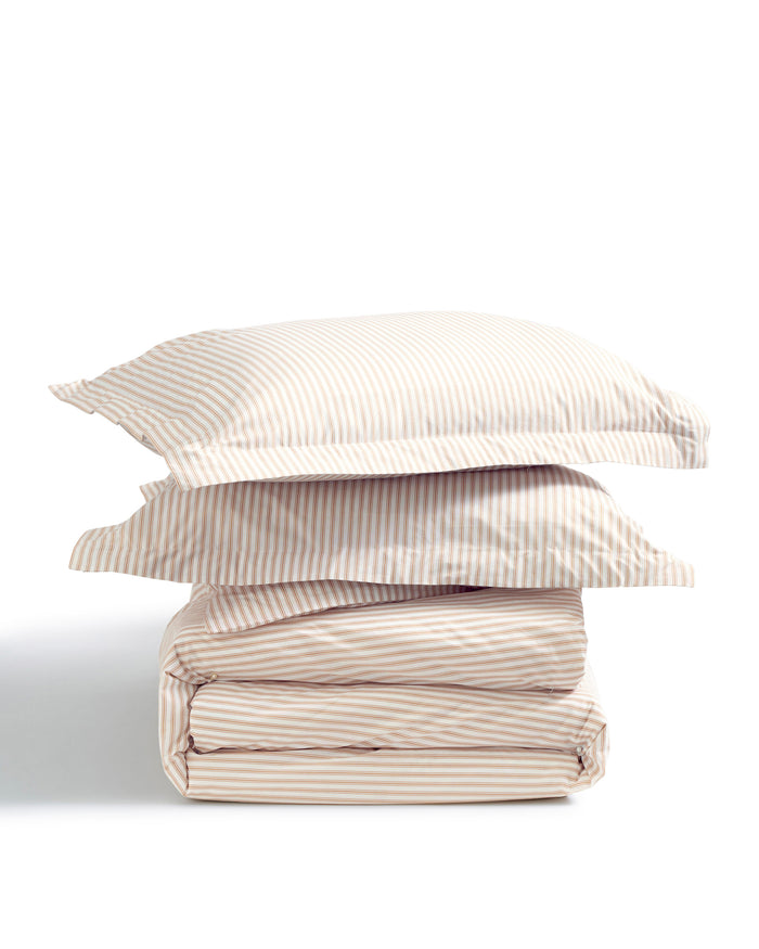 Two Luxe Premium Percale Duvet Set pillowcases in Camel Ticking Stripe are stacked on top of a folded matching sheet set, all arranged against a white background.