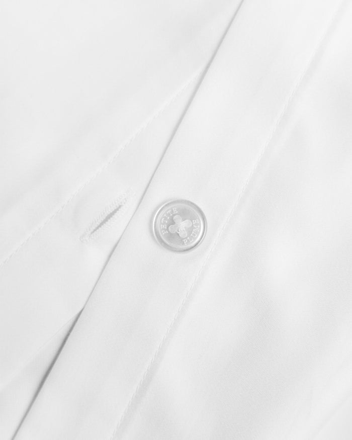 Close-up of the Petite Plume Luxe Premium Percale Duvet Set in White, showing a button and buttonhole. The smooth, neatly stitched fabric resembles luxury sheets, radiating a clean and crisp texture. The button is circular with four holes.
