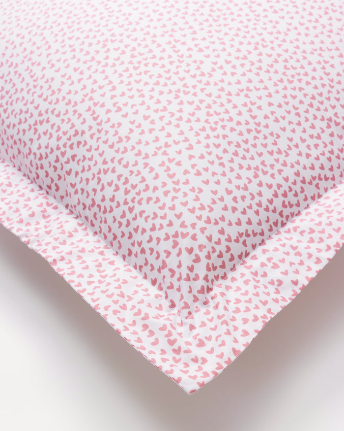 The Luxe Premium Percale Euro Sham in Sweethearts by Petite Plume is a cozy white pillow with a pink heart pattern and ruffled edge, crafted from percale fabric and shown against a white background.