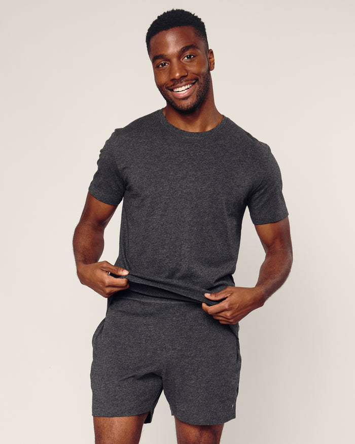 A man smiles against a light background, wearing Petite Plumes Mens 5 Pima Short in Dark Heather Grey and a matching Pima cotton short-sleeve tee. He holds the hem of his shirt with both hands.