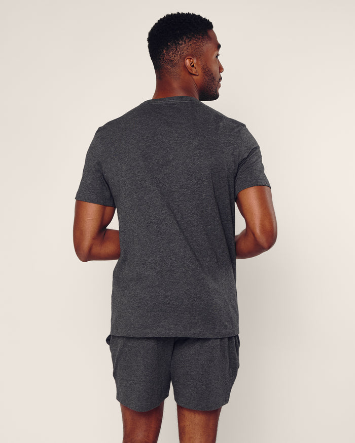 A man faces away from the camera, wearing Petite Plume’s Mens 5 Pima Short in Dark Heather Grey with a matching Peruvian Pima cotton short-sleeve shirt. The background is plain and light-colored.