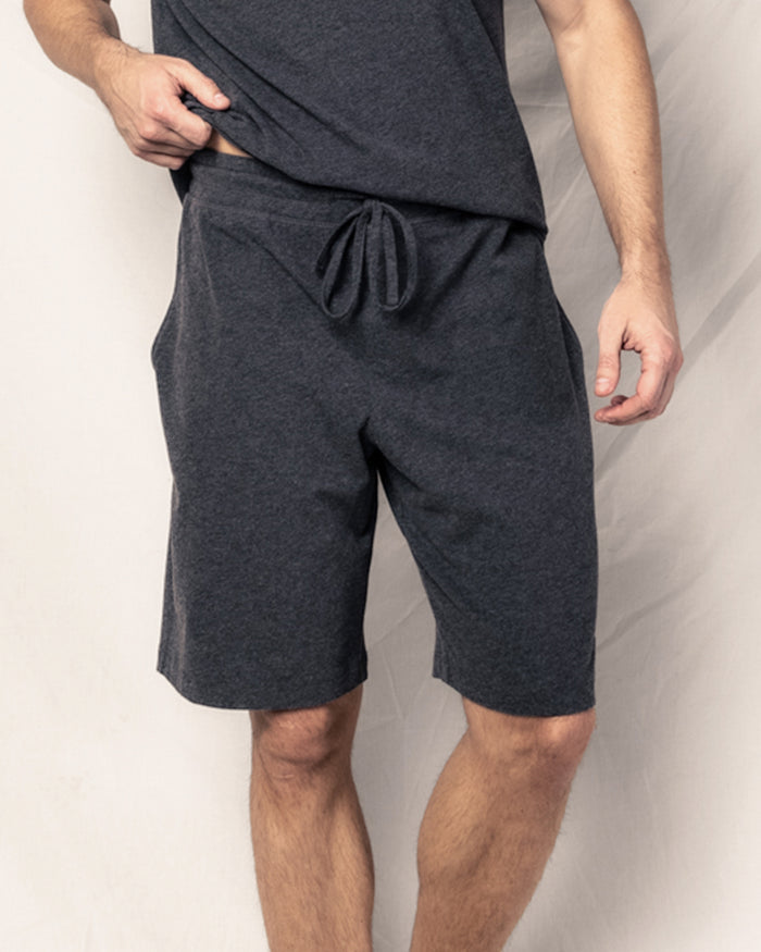 A person stands against a plain light background wearing Petite Plumes relaxed-fit Mens Classic Pima Shorts in Dark Heather Grey, crafted from soft Peruvian Pima cotton. Their face isnt visible.