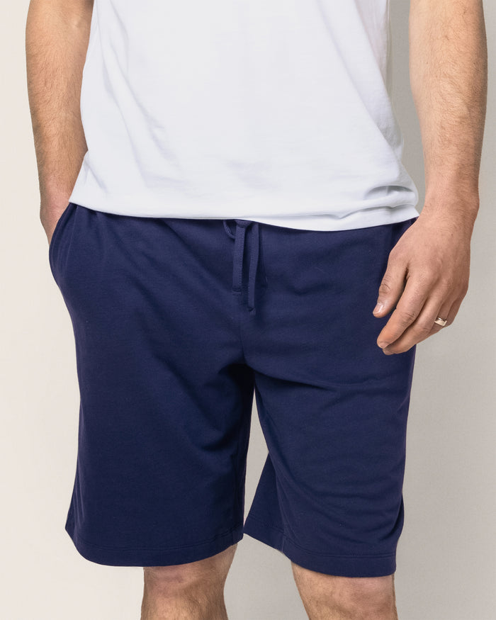 A person models Petite Plumes Mens Classic Pima Shorts in Navy and a plain white t-shirt made from luxurious Peruvian Pima cotton, exuding casual style ideal for a relaxed bedtime ritual. One hand stylishly rests in their pocket, emphasizing the outfits laid-back appeal.