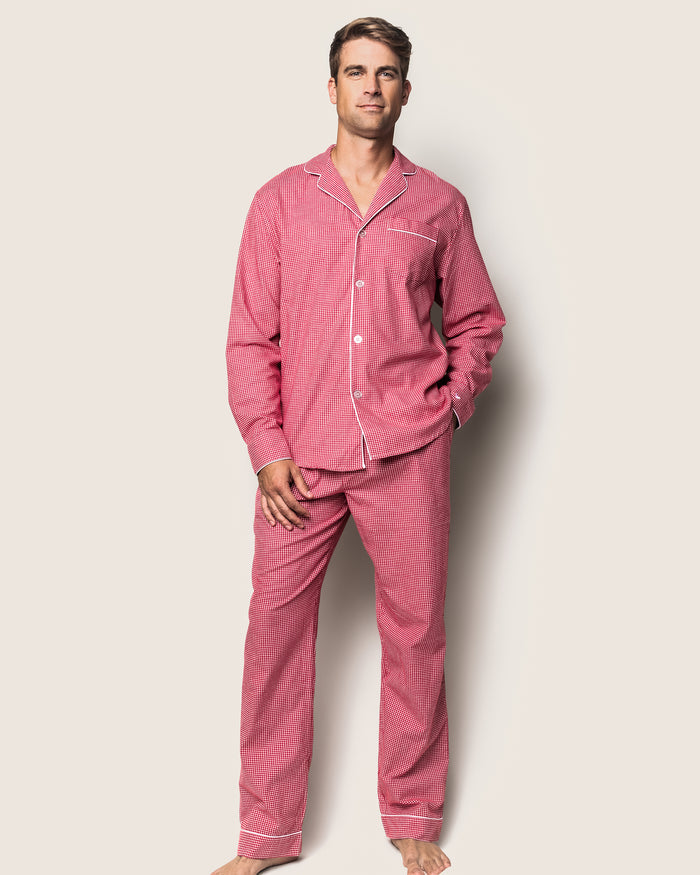 A person stands against a plain background wearing the Mens Flannel Pajama Set in Red Mini Gingham by Petite Plume, made from high-quality cotton. Their right hand is in the pants pocket as they appear relaxed and barefoot.