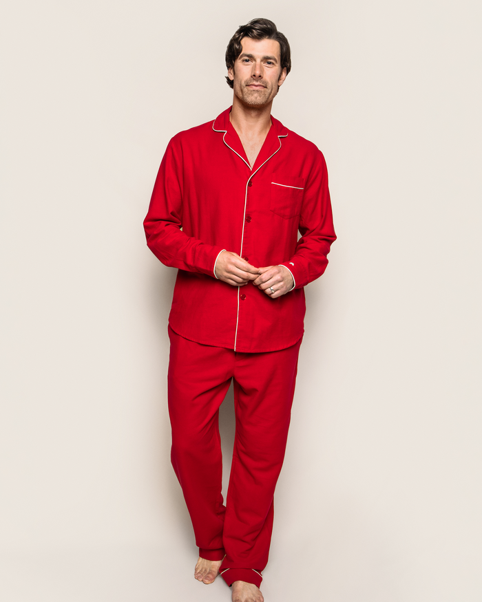 Against a plain backdrop, a person wears Petite Plumes Mens Flannel Pajama Set in red with white piping. Their dark hair and neutral expression highlight the elegance of the 100% cotton attire. Barefoot, they exude a relaxed and sophisticated vibe.