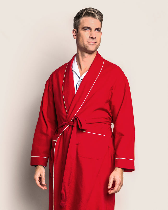 A person in a luxurious Mens Flannel Robe in Red with White Piping by Petite Plume stands against a light background, looking slightly to the side with one hand by their side and the other slightly bent.