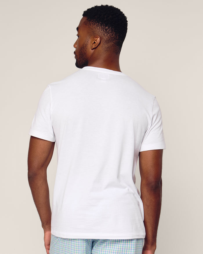 A person stands with their back to the camera, wearing Petite Plumes Mens Pima Crew Neck Short Sleeve Top in White and light-colored plaid pants made of soft Peruvian Pima cotton against an off-white background.