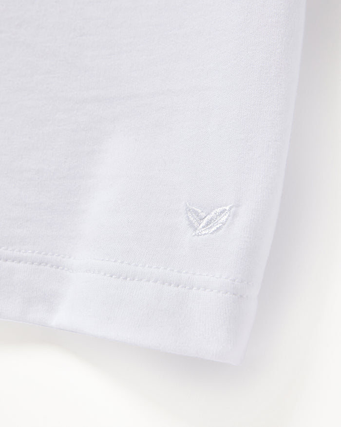 A close-up of the Mens Pima Crew Neck Short Sleeve Top in White by Petite Plume reveals luxurious Peruvian Pima cotton fabric with delicate stitching near the hem and a small white embroidered leaf on the smooth jersey knit.