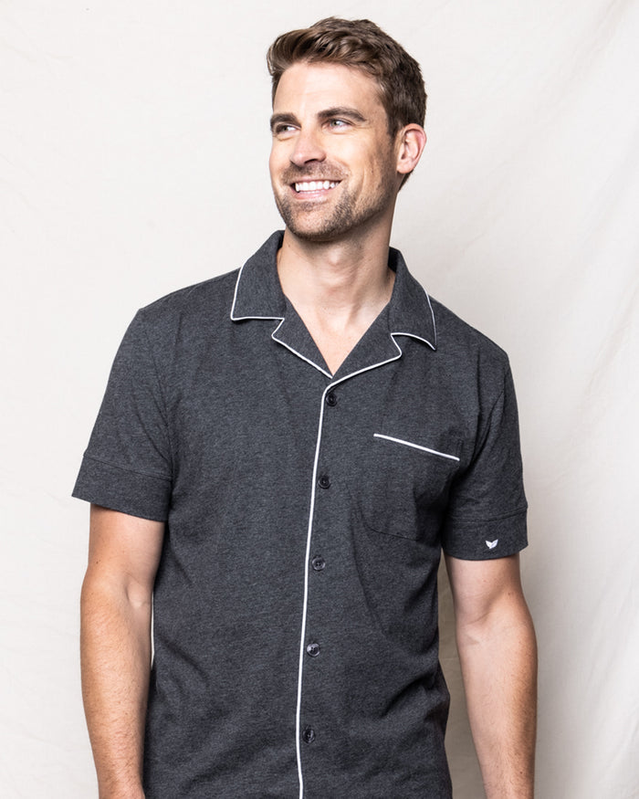 A man with short brown hair and light facial hair wears the Mens Pima Pajama Short Set in Dark Heather Grey by Petite Plume. He is smiling and looking to the side against a plain, light background.