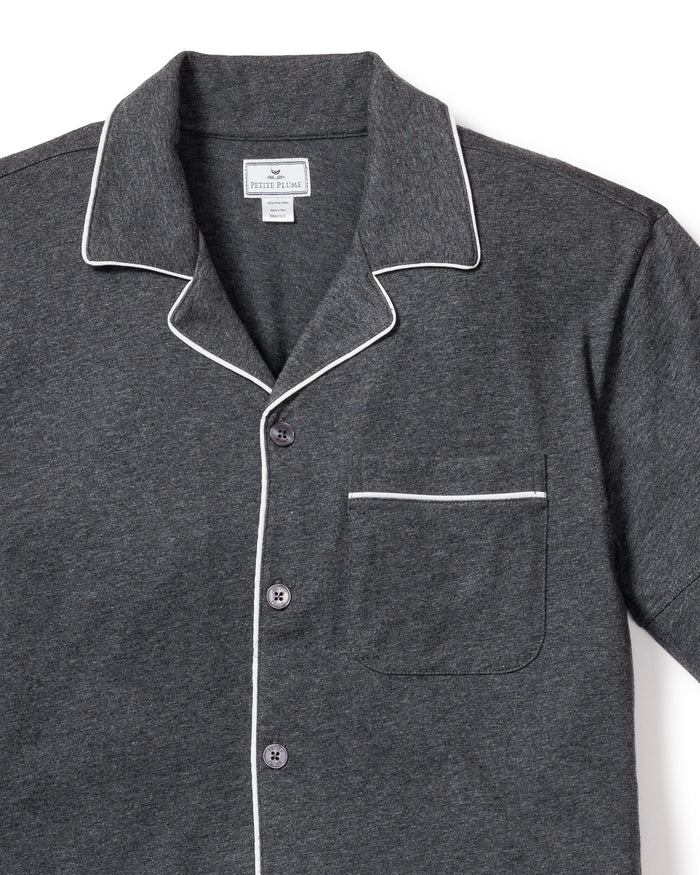 The Mens Pima Pajama Short Set by Petite Plume in Dark Heather Grey features a dark gray shirt with white piping on the collar, cuffs, and pocket outline. It includes a chest pocket and three buttons, made from soft yarn-dyed fabric, likely a cotton or Peruvian Pima cotton blend for a textured feel.