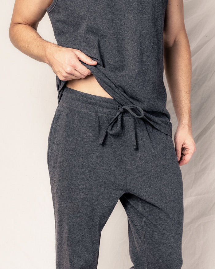 A person adjusts their clothing, wearing a sleeveless dark gray top and Petite Plumes Mens Pima Pants in Dark Heather Grey. Only their torso and upper legs are visible, with the pants drawstring untied against a plain light background.