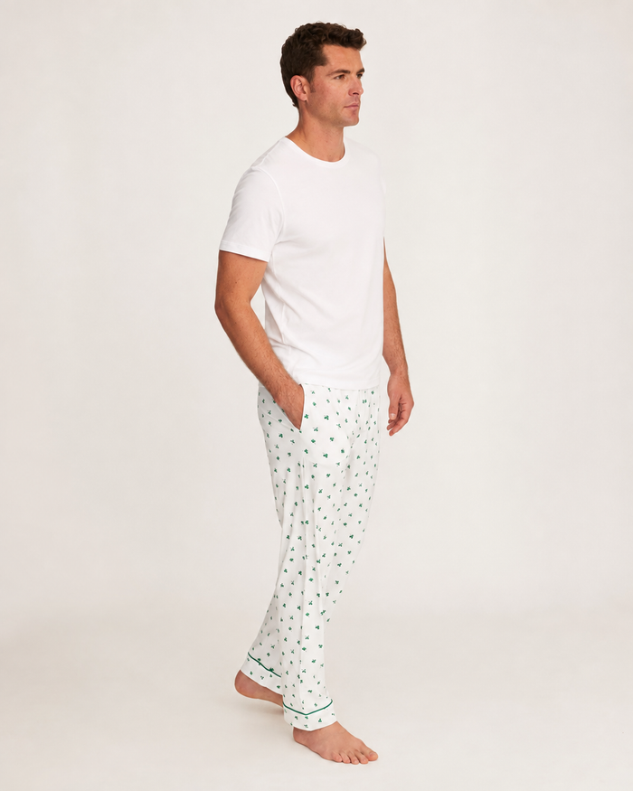 A man stands barefoot on a white background, wearing a plain white t-shirt and the Men’s Pima Pants in Shamrocks, with his hands in his pockets and looking off to the side.