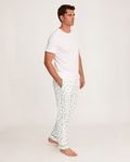 A man stands barefoot on a white background, wearing a plain white t-shirt and the Men’s Pima Pants in Shamrocks, with his hands in his pockets and looking off to the side.
