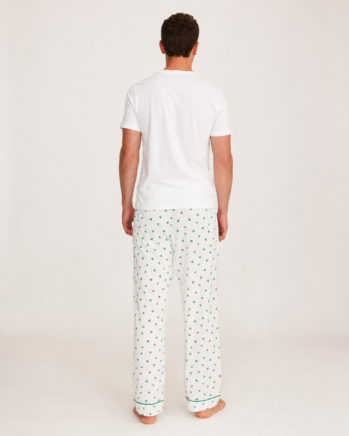 A man stands barefoot facing away, wearing a plain white T-shirt paired with Men’s Pima Pants in Shamrocks, on a light background.