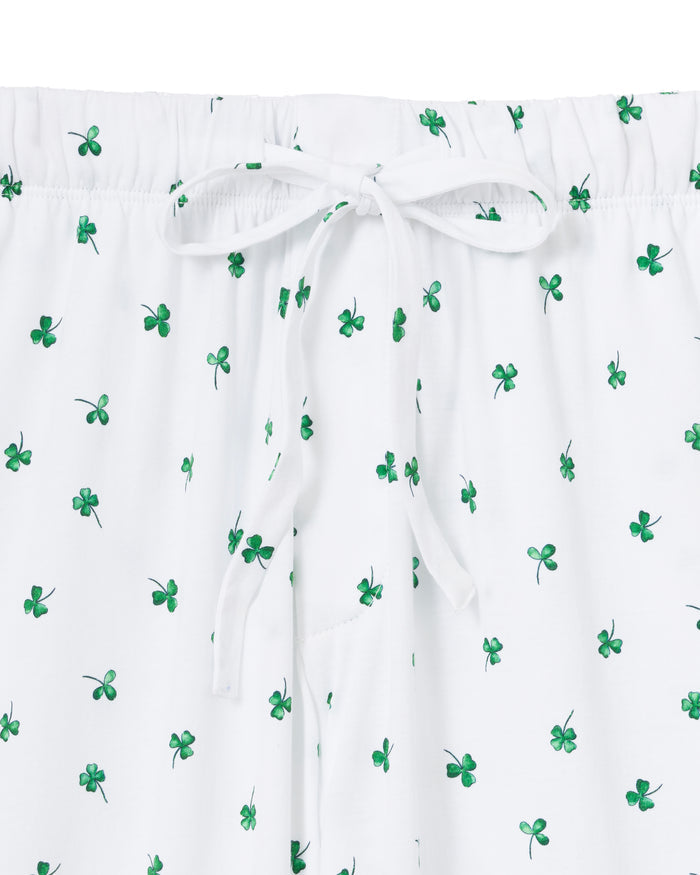 A man with short gray hair stands barefoot against a plain light background, wearing a plain white tee and Men's Pima Pants in Shamrocks—a white pajama pant with a small green pattern.