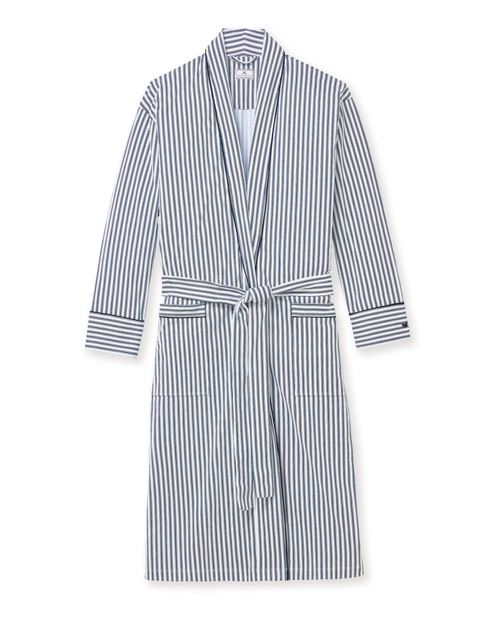 A man stands barefoot in white pajamas and the Men's Pima Robe in Navy French Ticking, belted, looking to the side against a plain light background.