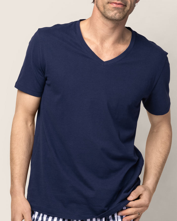 Against a plain background, a person wears Petite Plumes Mens Pima V-Neck Top in Navy and striped pants. Their hand rests on their hip, with part of their face out of frame.