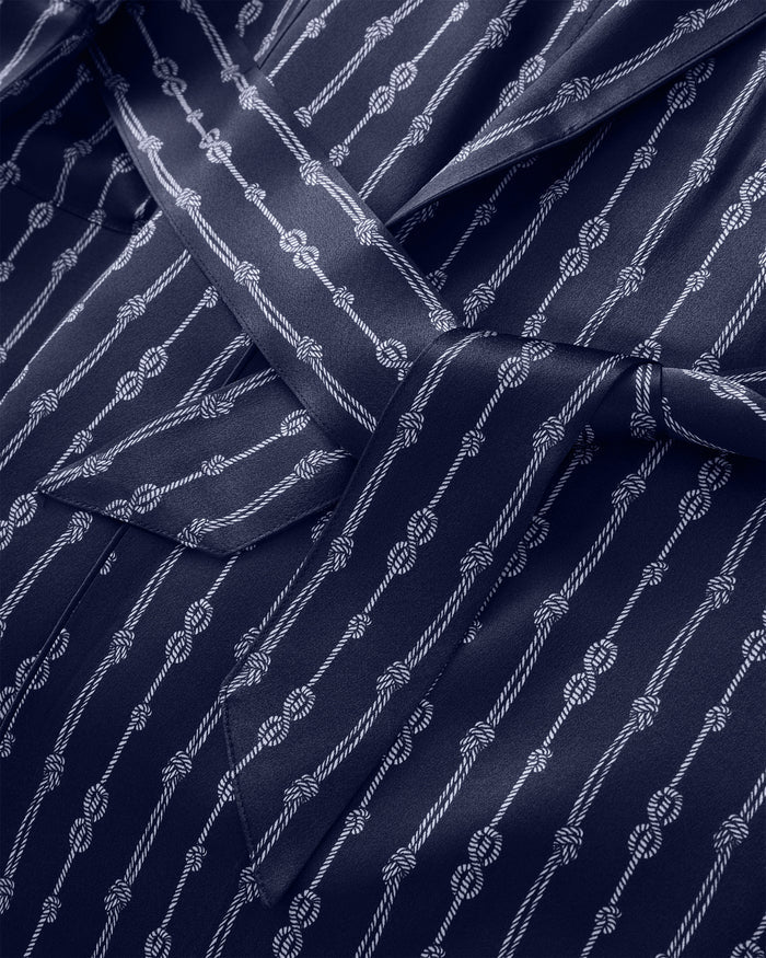 Close-up of the Men’s Silk Long Robe in Nautical Knots, featuring smooth, shiny navy blue silk adorned with a pattern of white ropes and knots. A belt is tied in a bow over a pocket.