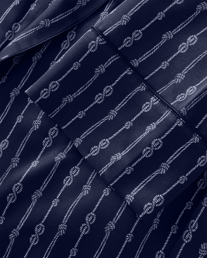 The image displays the Men’s Silk Long Robe in Nautical Knots, featuring navy blue silk adorned with a uniform pattern of white diagonal ropes and knots for a classic nautical look. Visible seams and folds highlight the garment’s elegant construction.