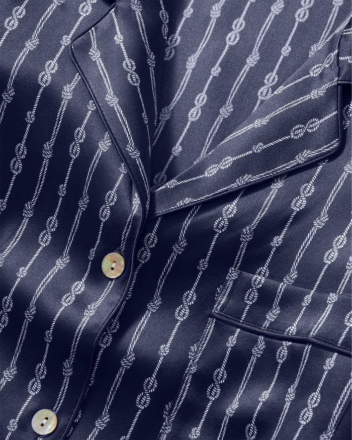 Close-up of the Men’s Silk Pajama Set in Nautical Knots, featuring a navy blue pajama shirt adorned with a white rope knot pattern, white buttons, and a front pocket. The silk fabric appears smooth and slightly shiny.