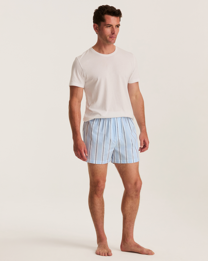 A man stands barefoot on a white background, wearing a plain white T-shirt and the Men’s Twill Boxers in Coastal Stripe.
