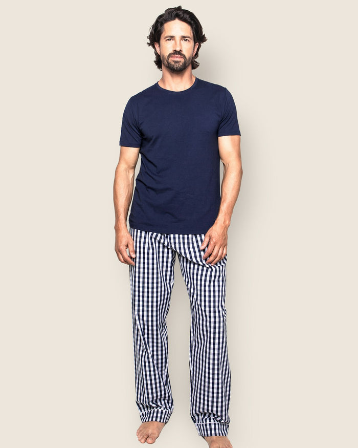A man with medium-length dark hair barefoot on a light background wears a navy t-shirt and Petite Plumes Men’s Twill Classic Navy Pajama Pant Duo, looking at the camera.