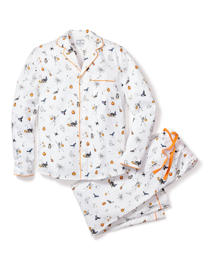 The Mens Twill Pajama Set in Trick or Treat by Petite Plume is made of premium cotton, featuring long sleeves and pants with a playful Halloween print of pumpkins, black cats, spiders, and bats, finished with orange trim and a decorative bow for a festive flair.