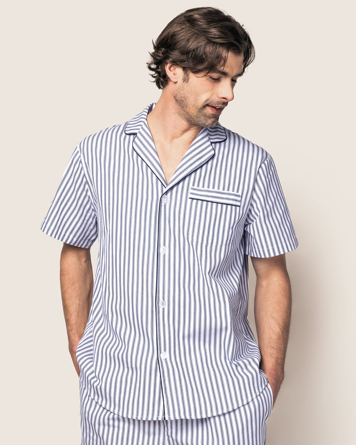 Indulge in the luxurious Mens Twill Pajama Short Set in Navy French Ticking by Petite Plume, featuring a short-sleeved button-up shirt with a pocket and matching shorts. Made from premium cotton, it showcases elegant blue and white stripes with a chic black drawstring on the shorts.