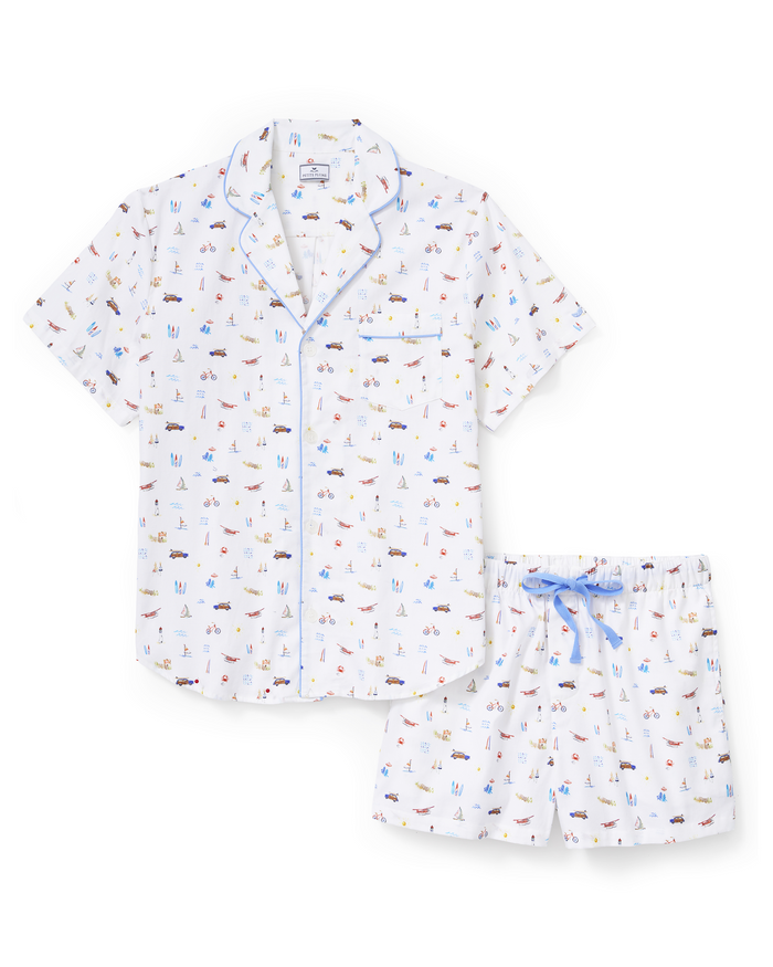 Men’s Twill Pajama Short Set in Summer Nostalgia, featuring a white short-sleeve shirt with blue piping and matching shorts with a light blue drawstring. The set is decorated with a beach-themed print showcasing small illustrations of people, boats, and various beach items.