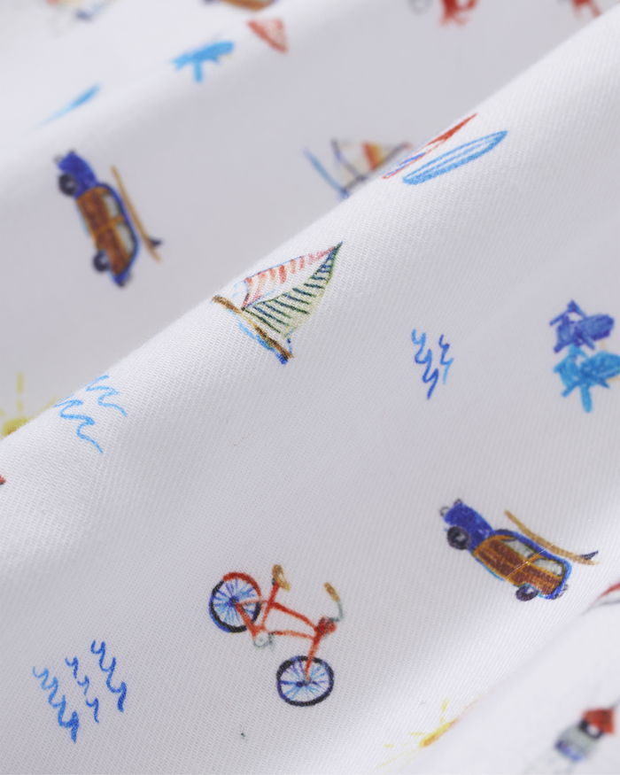 Men’s Twill Pajama Short Set in Summer Nostalgia features a white fabric adorned with playful, colorful illustrations of bicycles, cars with surfboards, boats, and waves. This scattered design creates a cheerful, nautical beach theme across the pajama set.