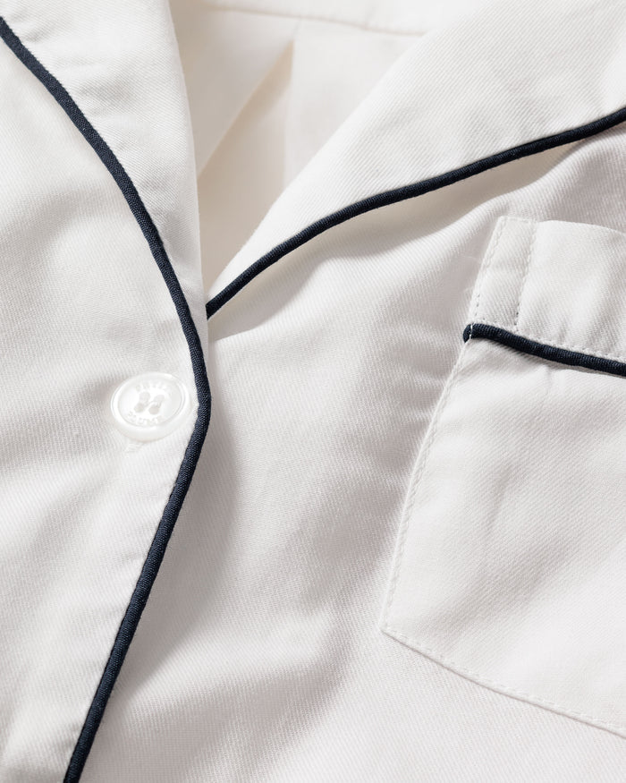Close-up of a cream-colored pajama shirt, part of Petite Plumes Mens Twill Pajama Short Set in White with Navy Piping. Made from 100% cotton, it includes a chest pocket and single white button, accentuated by contrasting trim for an elegant classic look.