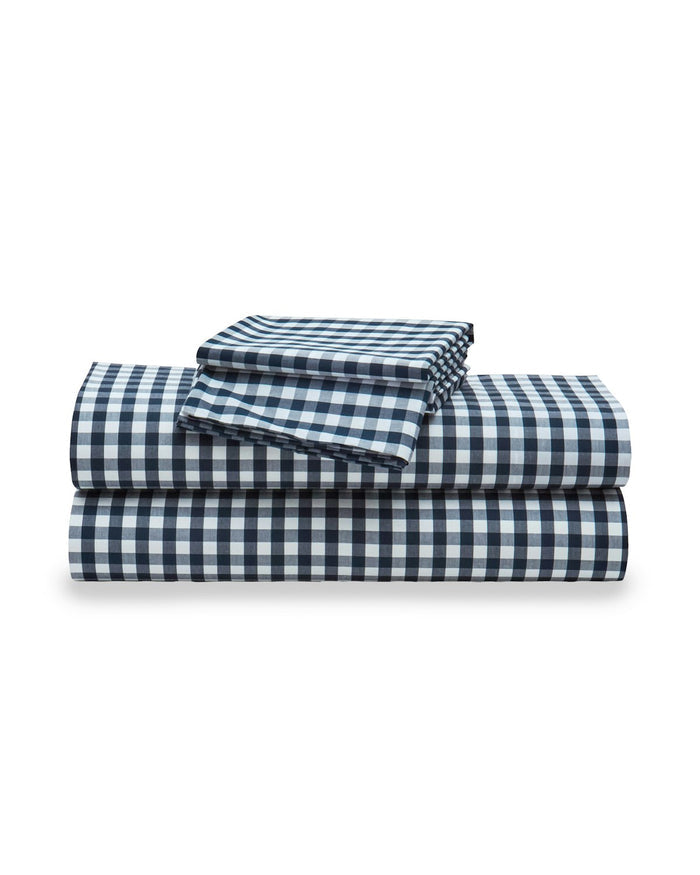 A neatly made bed featuring the Navy French Ticking and Navy Gingham Bedding Set on a wooden frame, with sunlight streaming onto the wall behind.