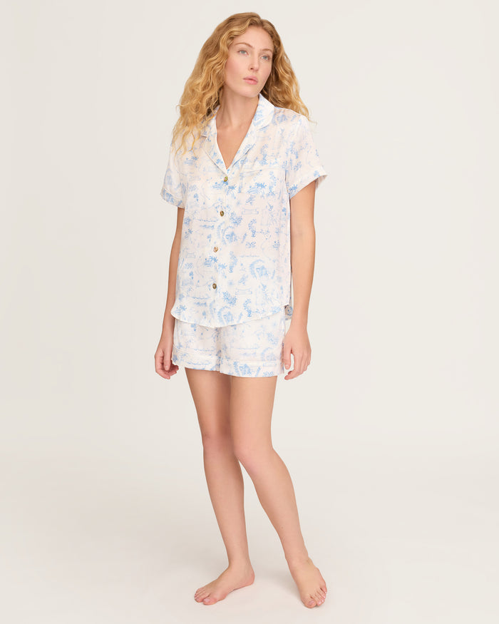 The Petite Plume x Eden Rock Blue Reverie Women's Silk Short Set features a white base with light blue nature-inspired prints, a short-sleeve button-up shirt with chest pocket, and drawstring waist shorts.