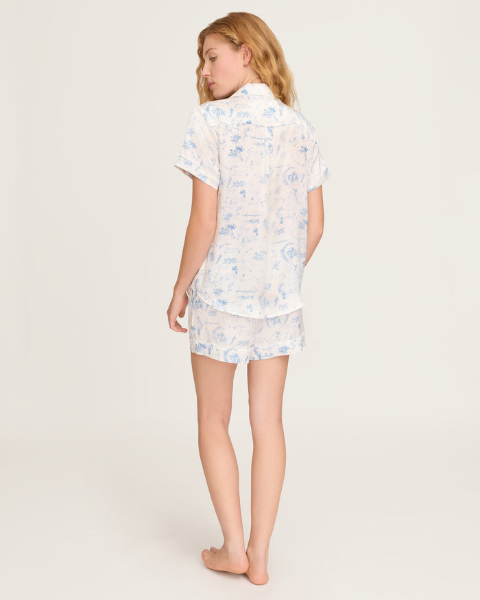 The Petite Plume x Eden Rock Blue Reverie Women's Silk Short Set features a white base with light blue nature-inspired prints, a short-sleeve button-up shirt with chest pocket, and drawstring waist shorts.