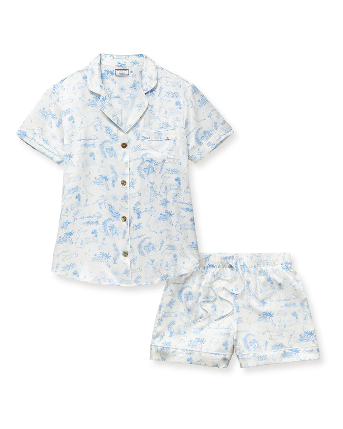 The Petite Plume x Eden Rock Blue Reverie Women's Silk Short Set features a white base with light blue nature-inspired prints, a short-sleeve button-up shirt with chest pocket, and drawstring waist shorts.