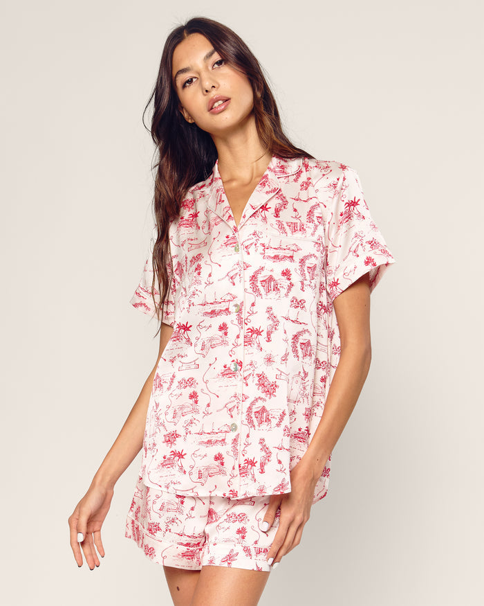The Petite Plume x Eden Rock Reverie Women’s Silk Short Set features a short-sleeve button-up shirt and shorts with a white background and red toile print of scenic and floral patterns.