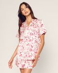 The Petite Plume x Eden Rock Reverie Women’s Silk Short Set features a short-sleeve button-up shirt and shorts with a white background and red toile print of scenic and floral patterns.