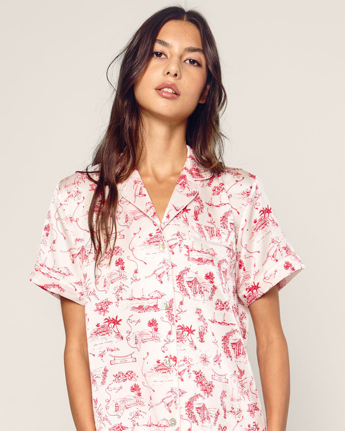 The Petite Plume x Eden Rock Reverie Women’s Silk Short Set features a short-sleeve button-up shirt and shorts with a white background and red toile print of scenic and floral patterns.