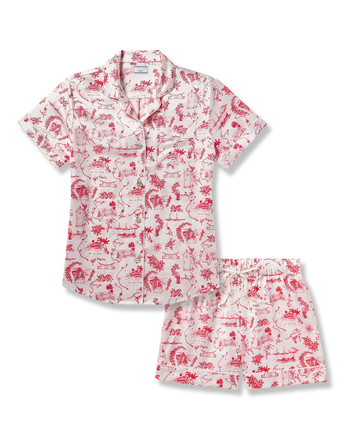 The Petite Plume x Eden Rock Reverie Women’s Silk Short Set features a short-sleeve button-up shirt and shorts with a white background and red toile print of scenic and floral patterns.