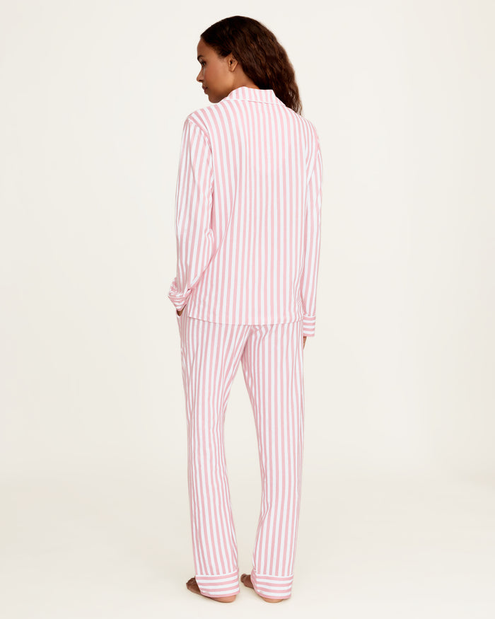 The Petite Plume x Eloise Women's Pima Pajama Set in Eloise Classic Stripe features pink and white vertical stripes, a long-sleeve button-up top with a collar, chest pocket with red embroidery, and matching pants.