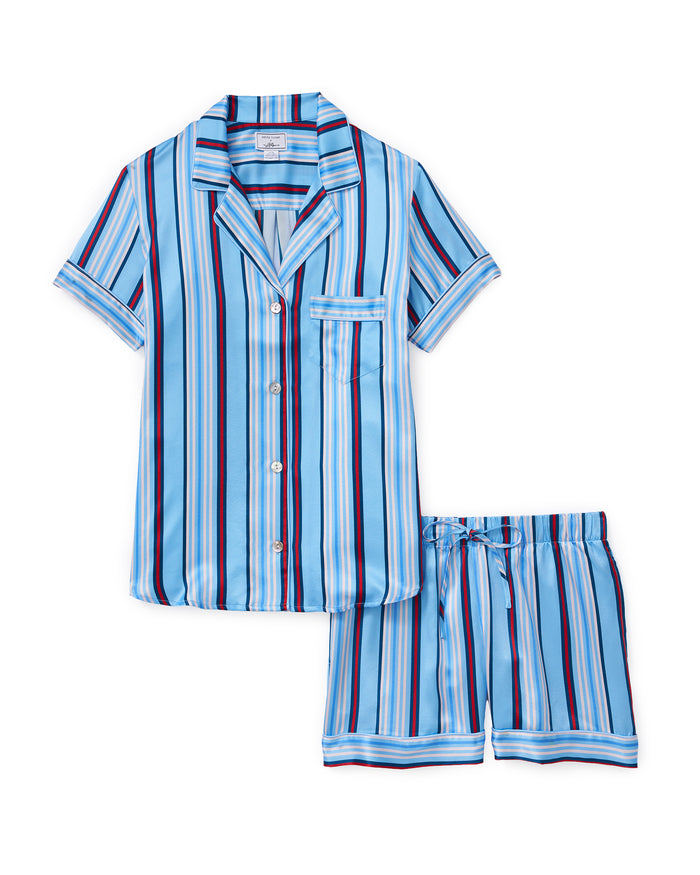 The Petite Plume x Hedges Women’s Silk Short Set in Blue Stripe features a blue silk short-sleeve top with vertical navy, black, white, and red stripes, complete with a chest pocket and button front. The matching shorts offer an elastic waistband for comfort.