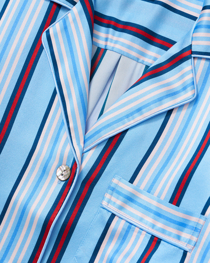 Close-up of the Petite Plume x Hedges Women’s Silk Short Set in Blue Stripe, featuring a button-up pajama shirt with blue, white, red, and light pink stripes, a front pocket, a collar, and crafted from silky fabric.