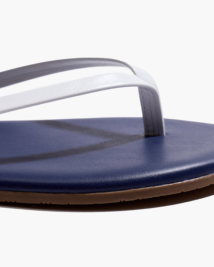 A pair of Petite Plume x TKEES Lily Sandals in navy with white straps, photographed from above on a white background. "THE PETITE PLUME" is printed in gold on the insoles.