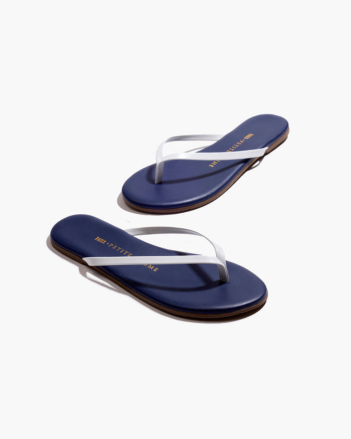 A pair of Petite Plume x TKEES Lily Sandals in navy with white straps, photographed from above on a white background. "THE PETITE PLUME" is printed in gold on the insoles.